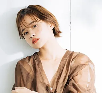 茶髪のショートボブの女性が壁にもたれる様子