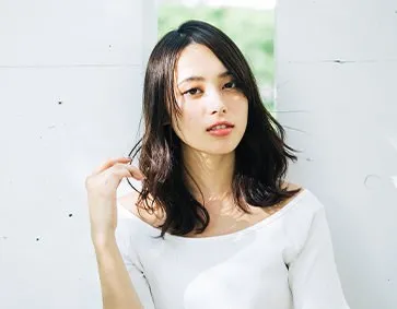 白い壁の前で髪に触れるミディアムヘアの女性