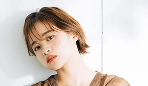茶髪のショートボブの女性が壁にもたれる様子